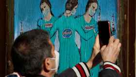 Un hombre fotografía un mural con 'las tres vacunas' en Barcelona.