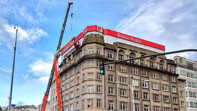 La grúa retira del edificio del Banco Santander de Cuatro Caminos el letrero del Pastor.