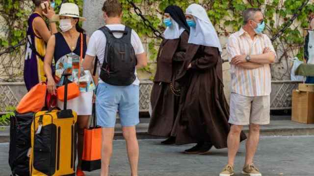 Turistas en Sevilla mientras dos hermanas de la Cruz pasan por detrás con mascarillas.