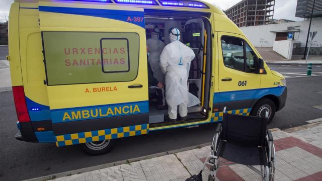 Un trabajador sanitario totalmente protegido ayuda a subir a la ambulancia a un anciano.