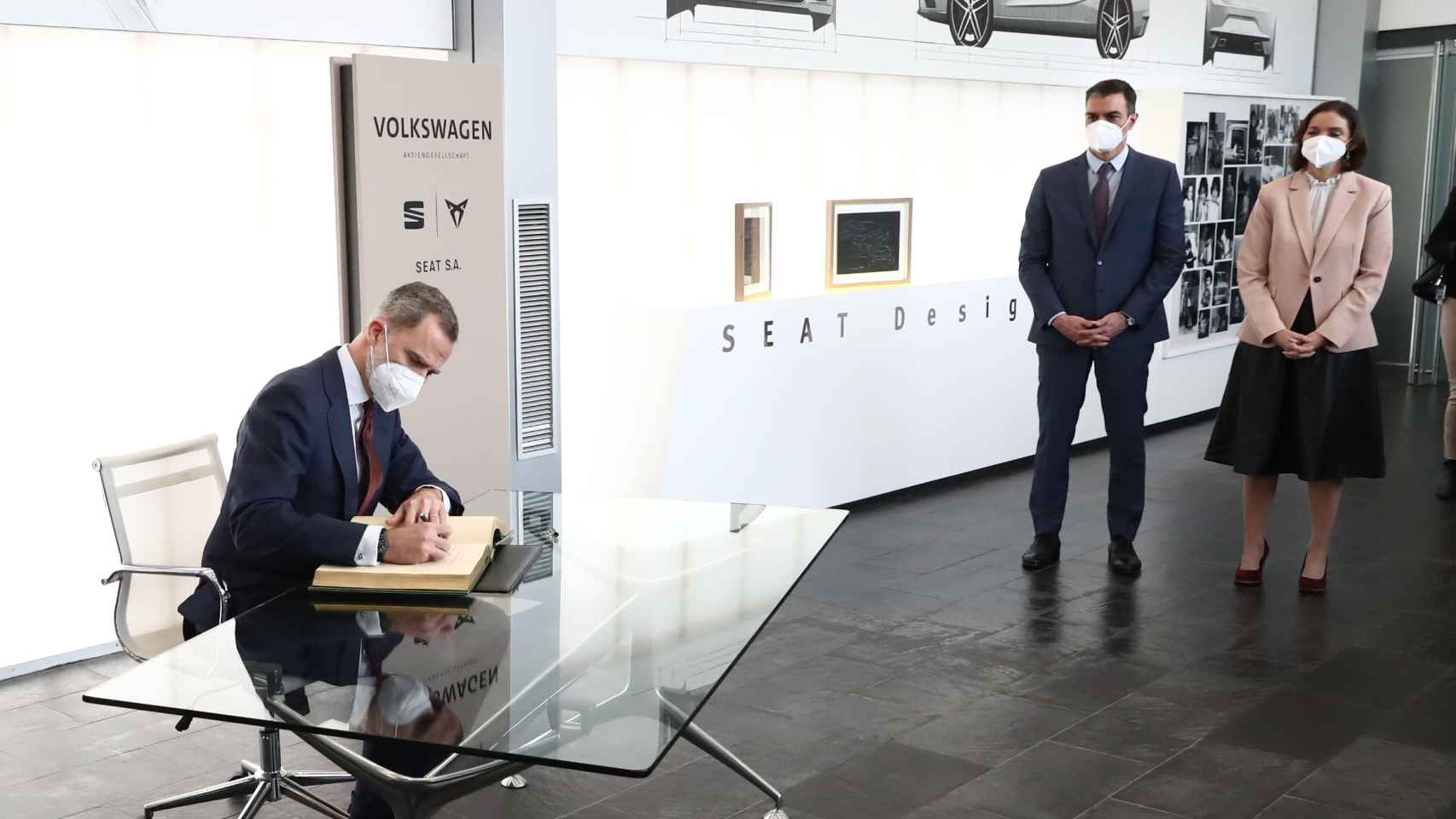 Felipe VI firma en el libro de honor de la fábrica de Seat en Martorell (Barcelona), ante Pedro Sánchez y Reyes Maroto.