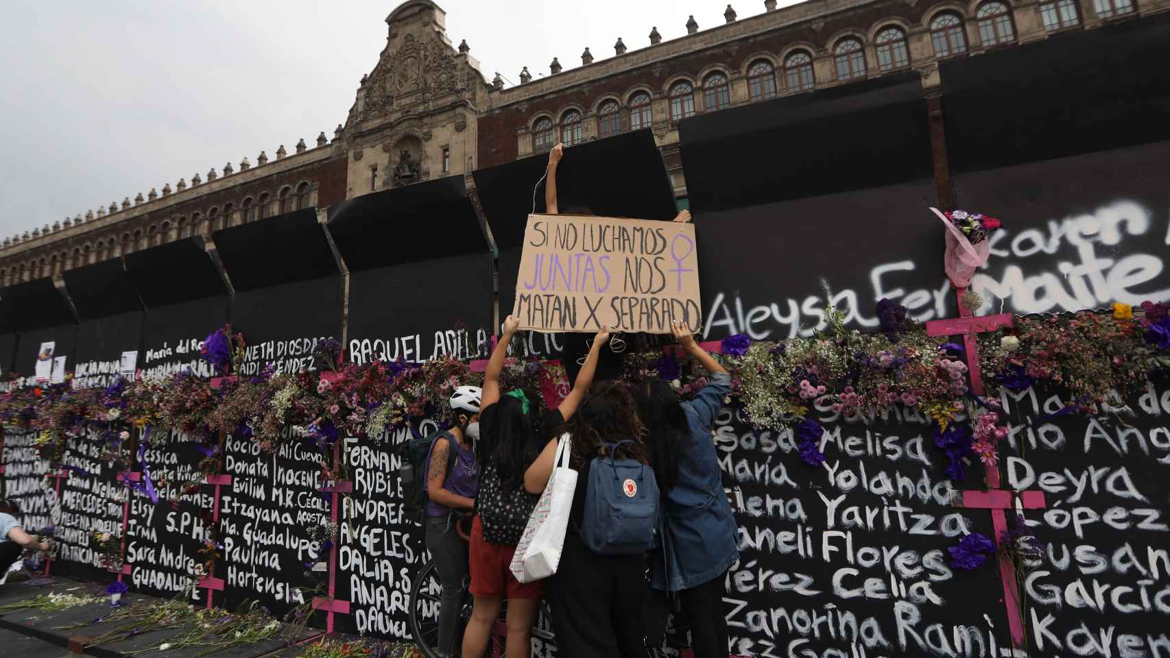 Mujeres colocan flores y carteles en la valla frente al Palacio Nacional de México.