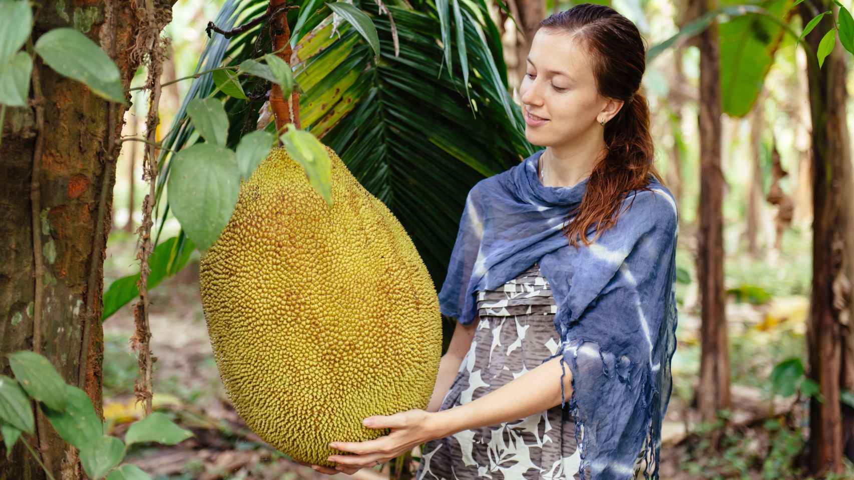 Una mujer junto a un ejemplar de jackfruit muy grande.