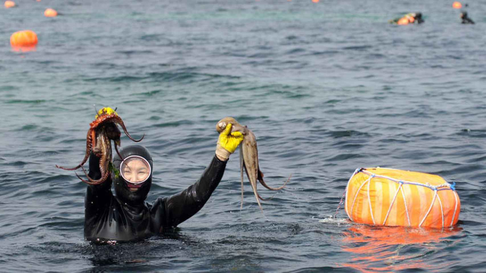 Una mujer del mar sale a la superficie con un par de pulpos que ha capturado.