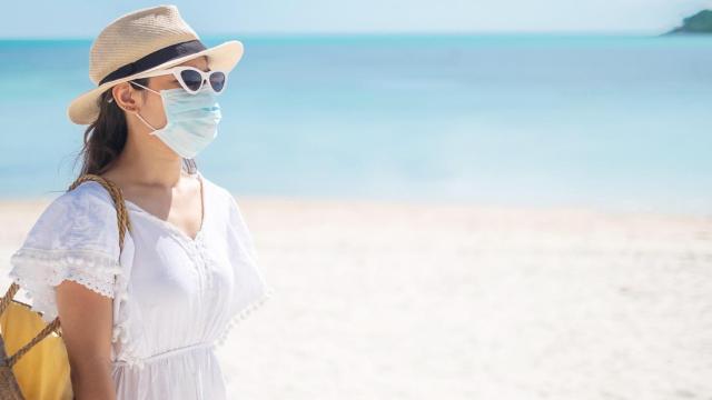 Una mujer camina por la playa con la mascarilla puesta.