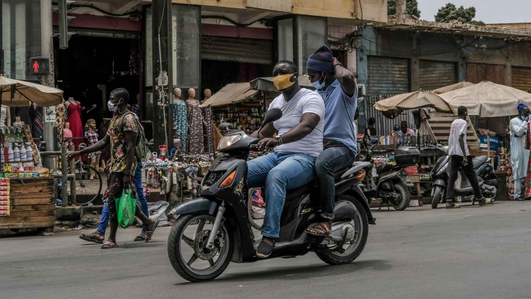 Dos hombres con mascarilla en una moto en Dakar.