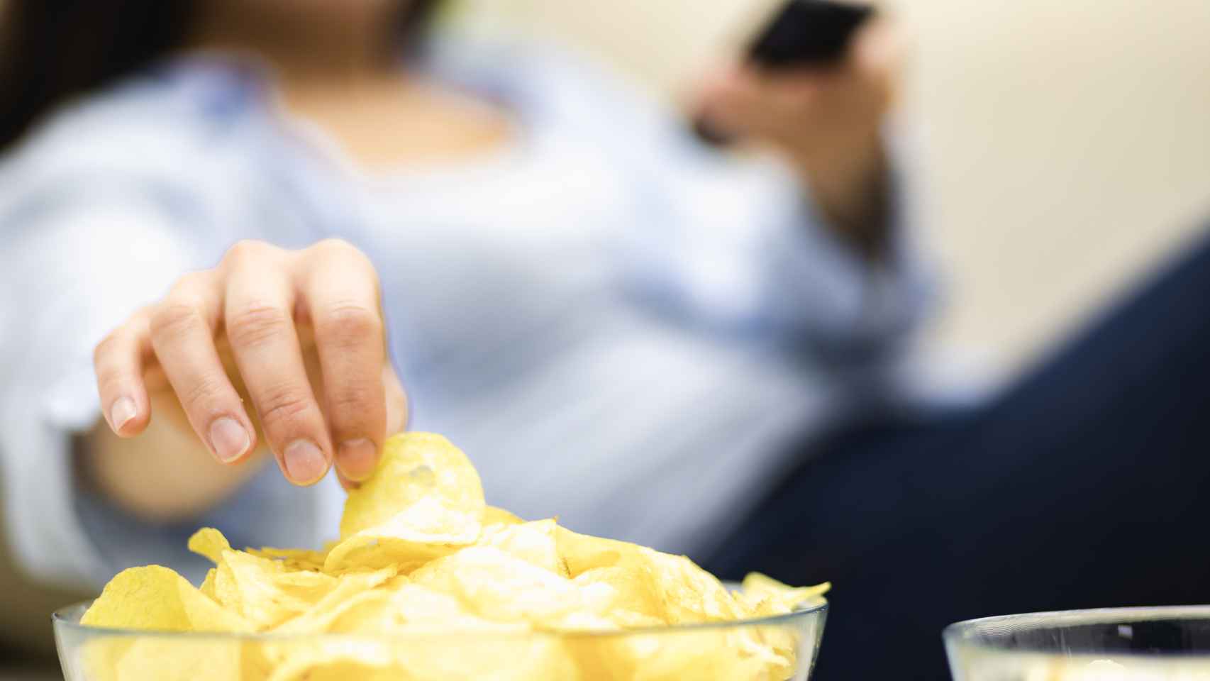 Una mujer toma patatas fritas mientras consulta su móvil.