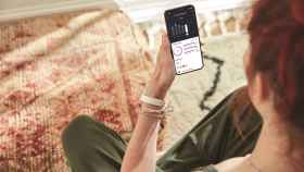 Una mujer con la pulsera de Fitbit, consultando sus datos personales en el smartphone