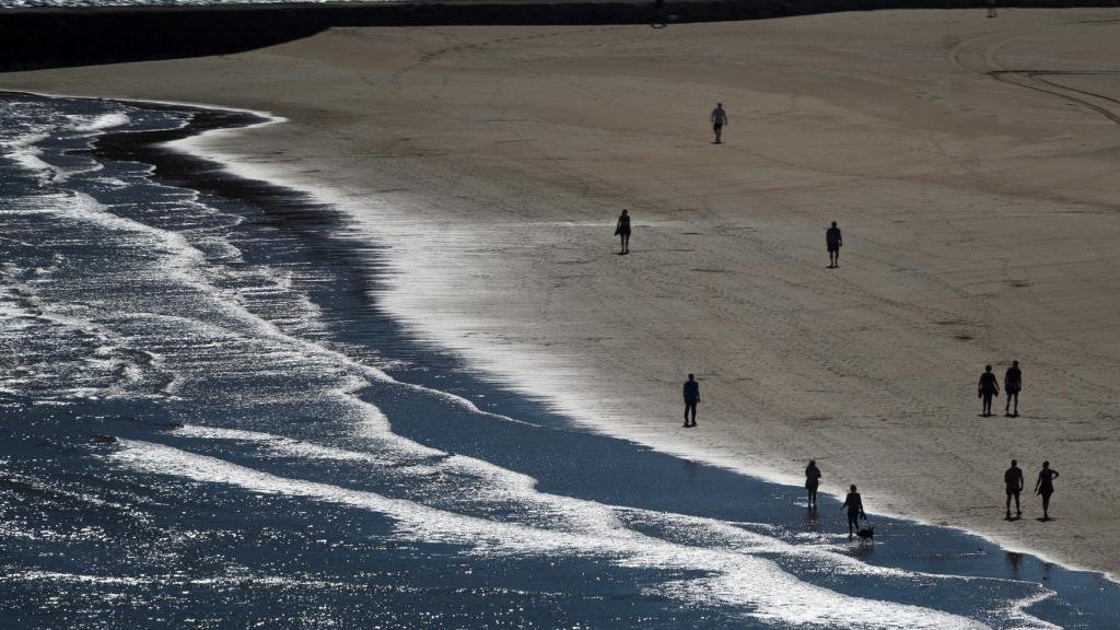 Varias personas pasean por la playa La Concha este viernes en la localidad cántabra de Suances.