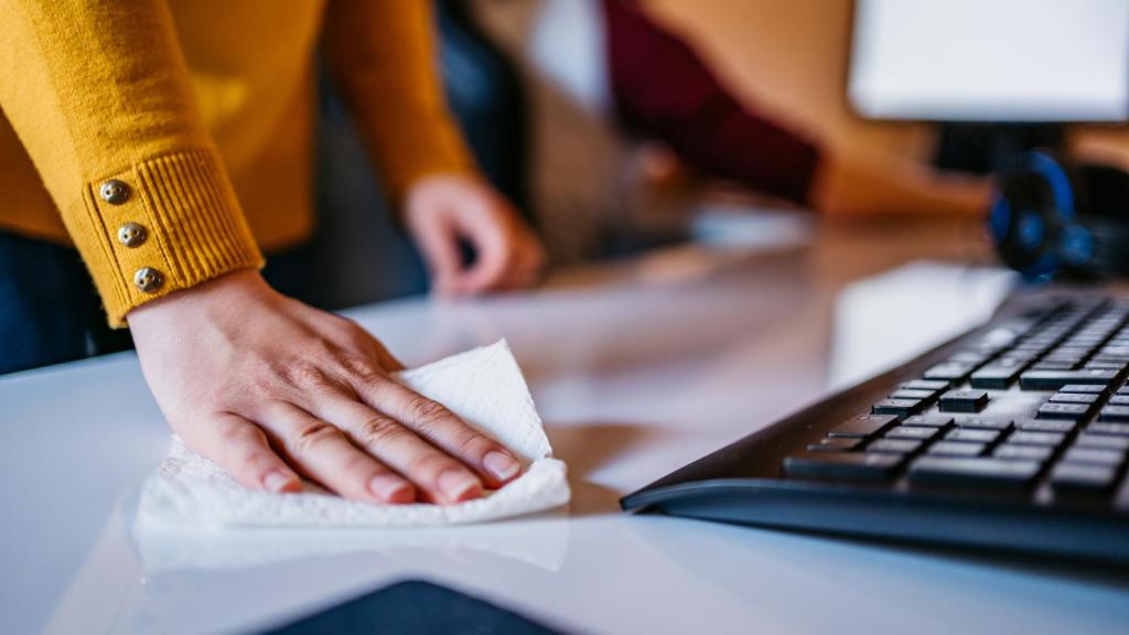 Una persona higieniza la mesa de trabajo.