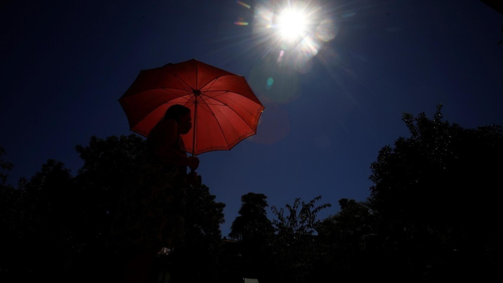 Una joven pasea bajo el sol con un paraguas.