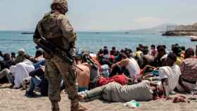 Inmigrantes sentados en la playa de El Tarajal, de Ceuta, ante un soldado español.
