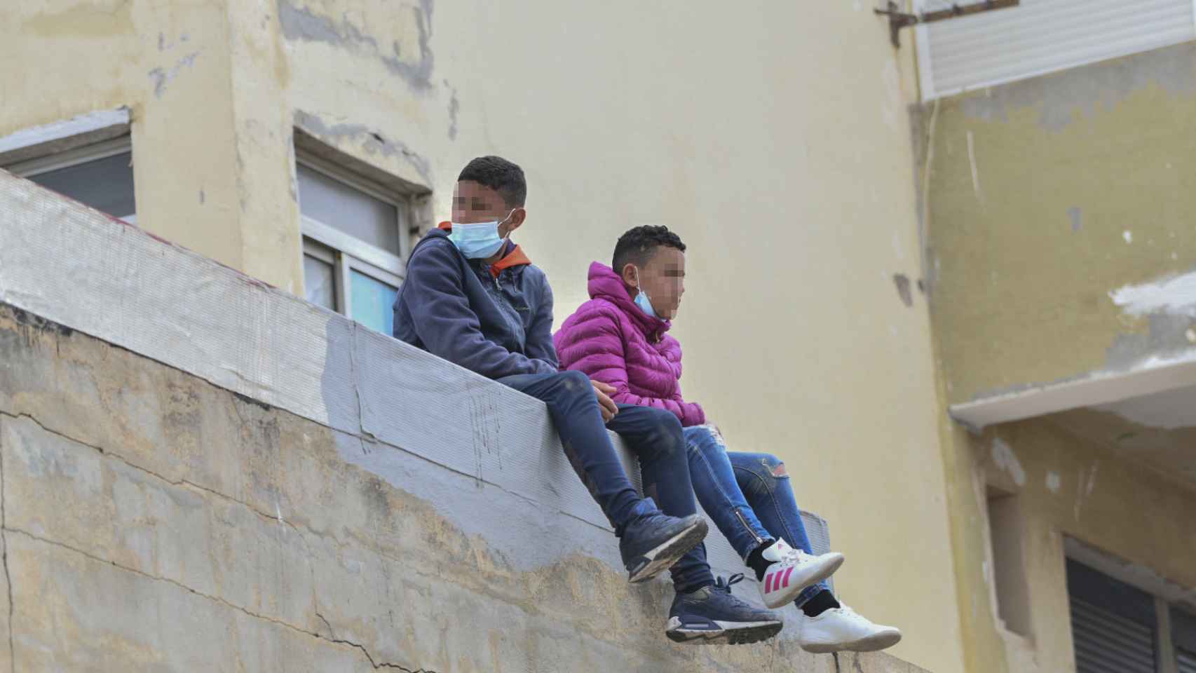 Dos niños sentados sobre un muro en la nave de primera acogida del polígono del Tarajal, en Ceuta. EP