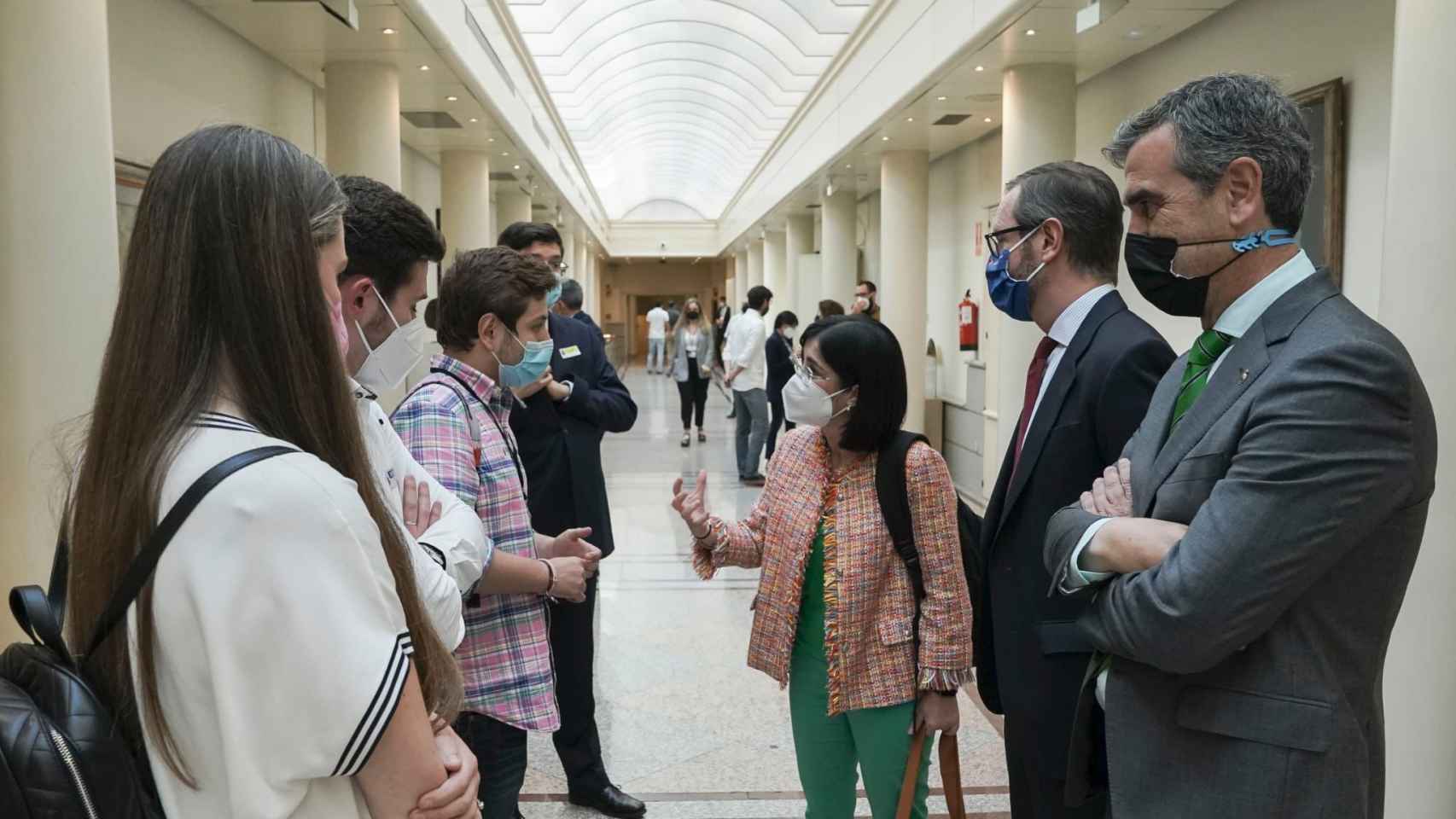 La ministra de Sanidad junto con algunos MIR en los pasillos del Senado y acompañada del portavoz de PP, Antonio Román.