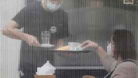 Un camarero sirve a una mesa tras una mampara.