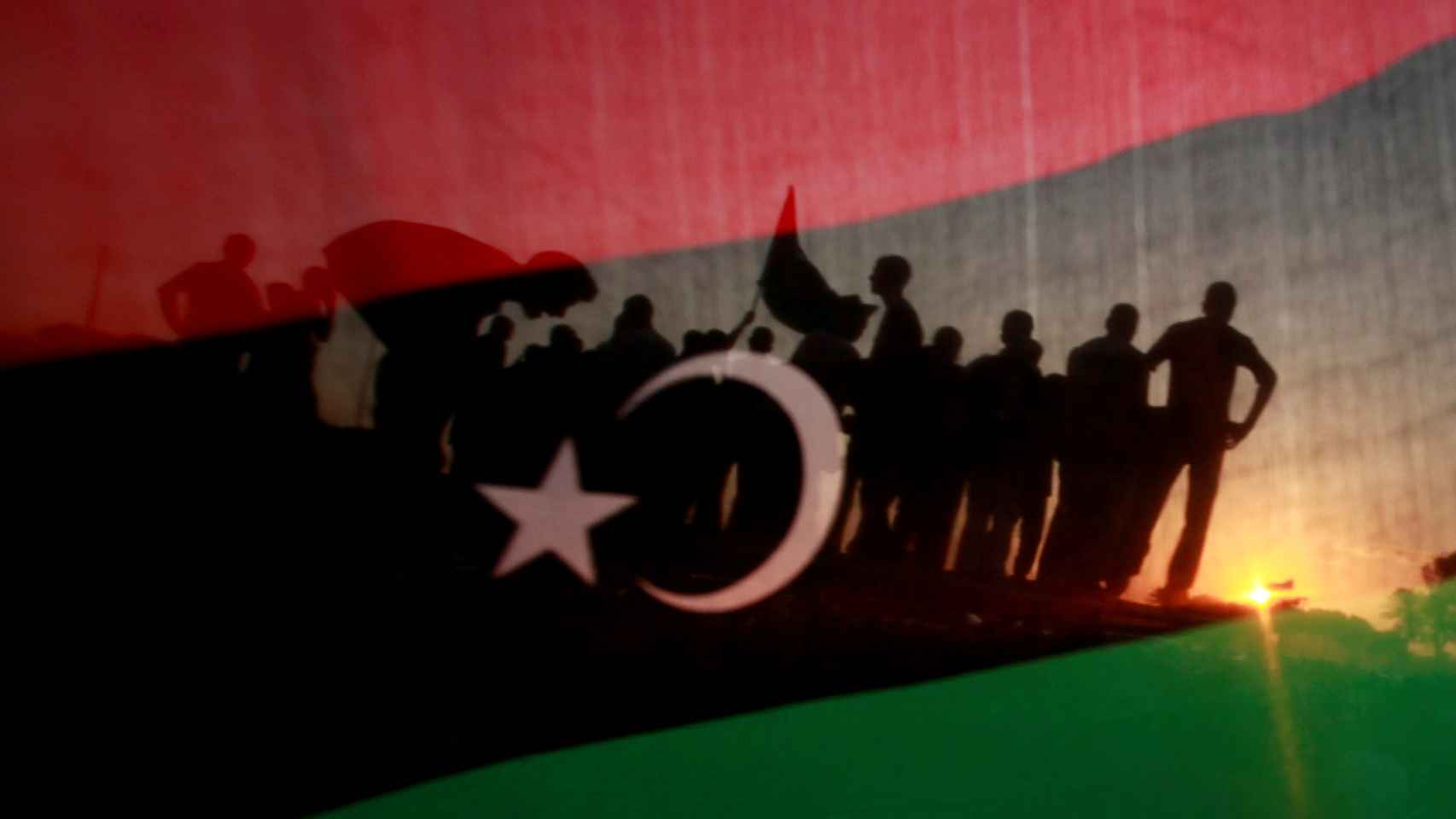 Un grupo de libios apostados frente a la casa de Muamar el Gadafi y vistos a través de una bandera Libia.