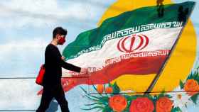 Un chico iraní pasa junto a un mural con la bandera nacional de Irán en una calle de Teherán.
