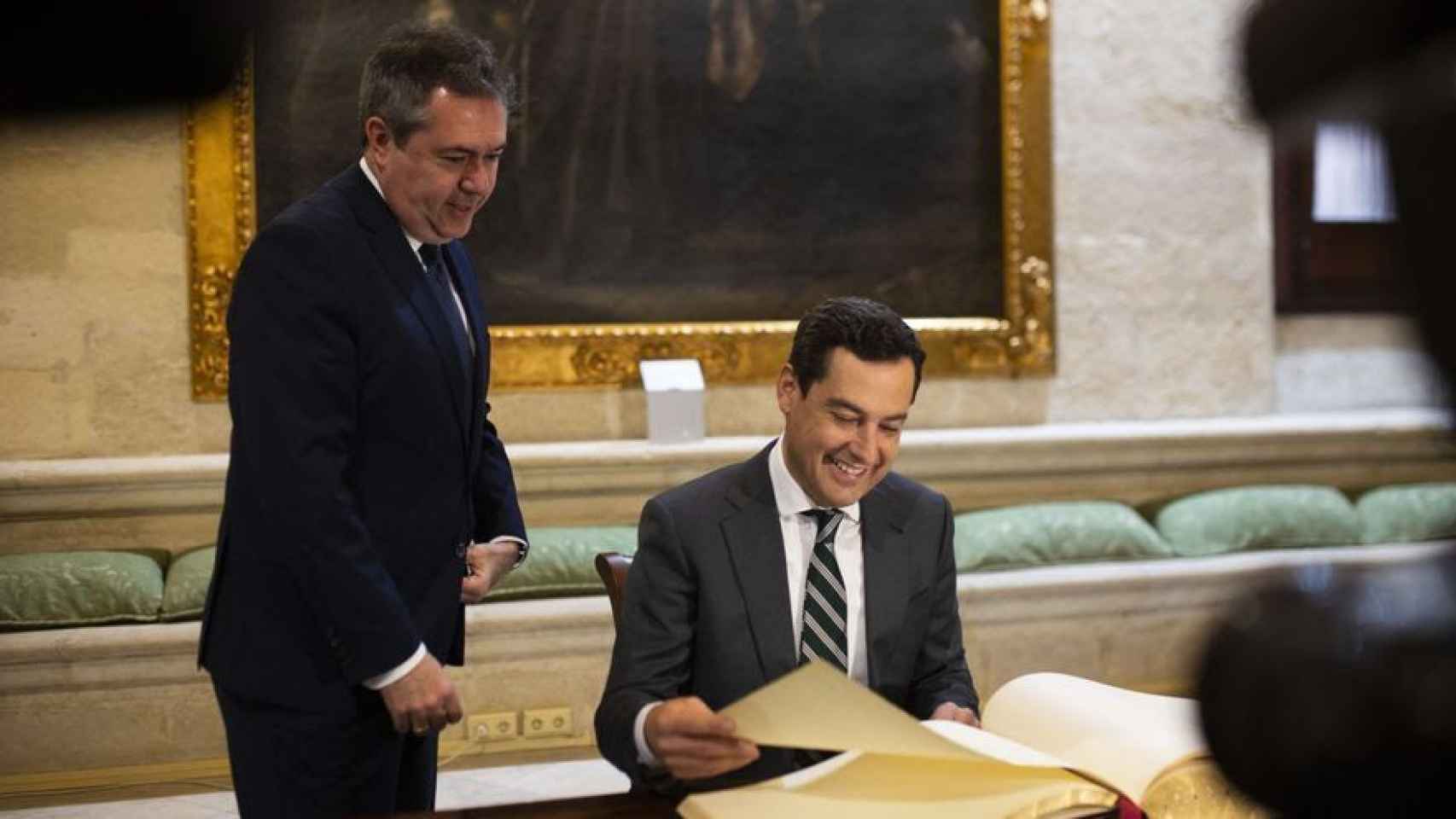 Juanma Moreno firma en el libro de visitas del Ayuntamiento de Sevilla junto a Juan Espadas.
