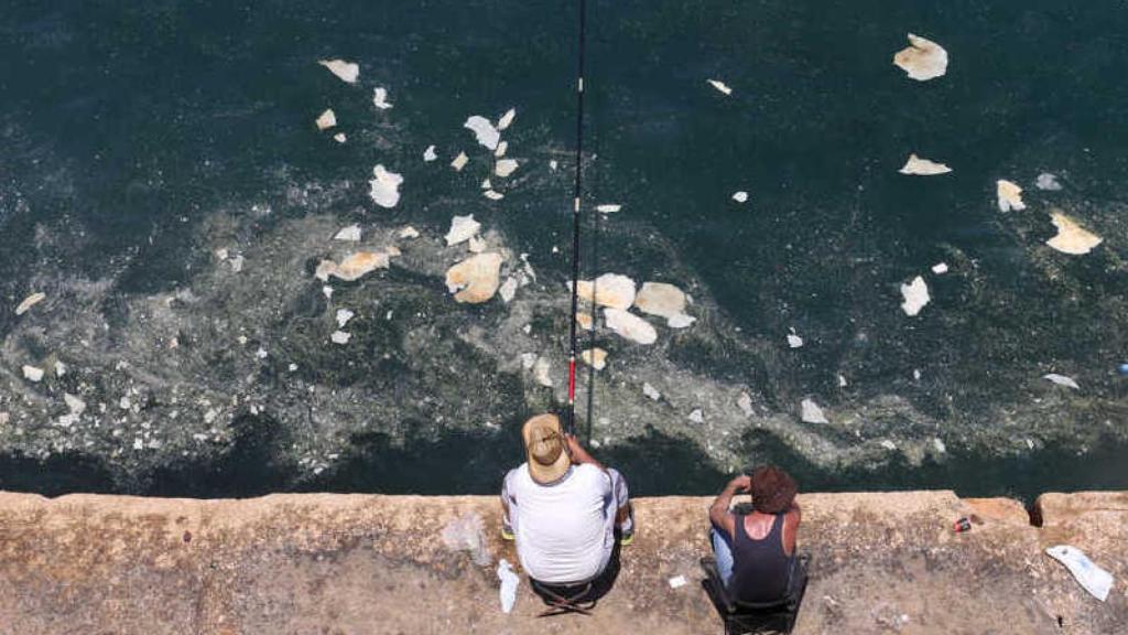Dos personas pescan en aguas contaminadas.