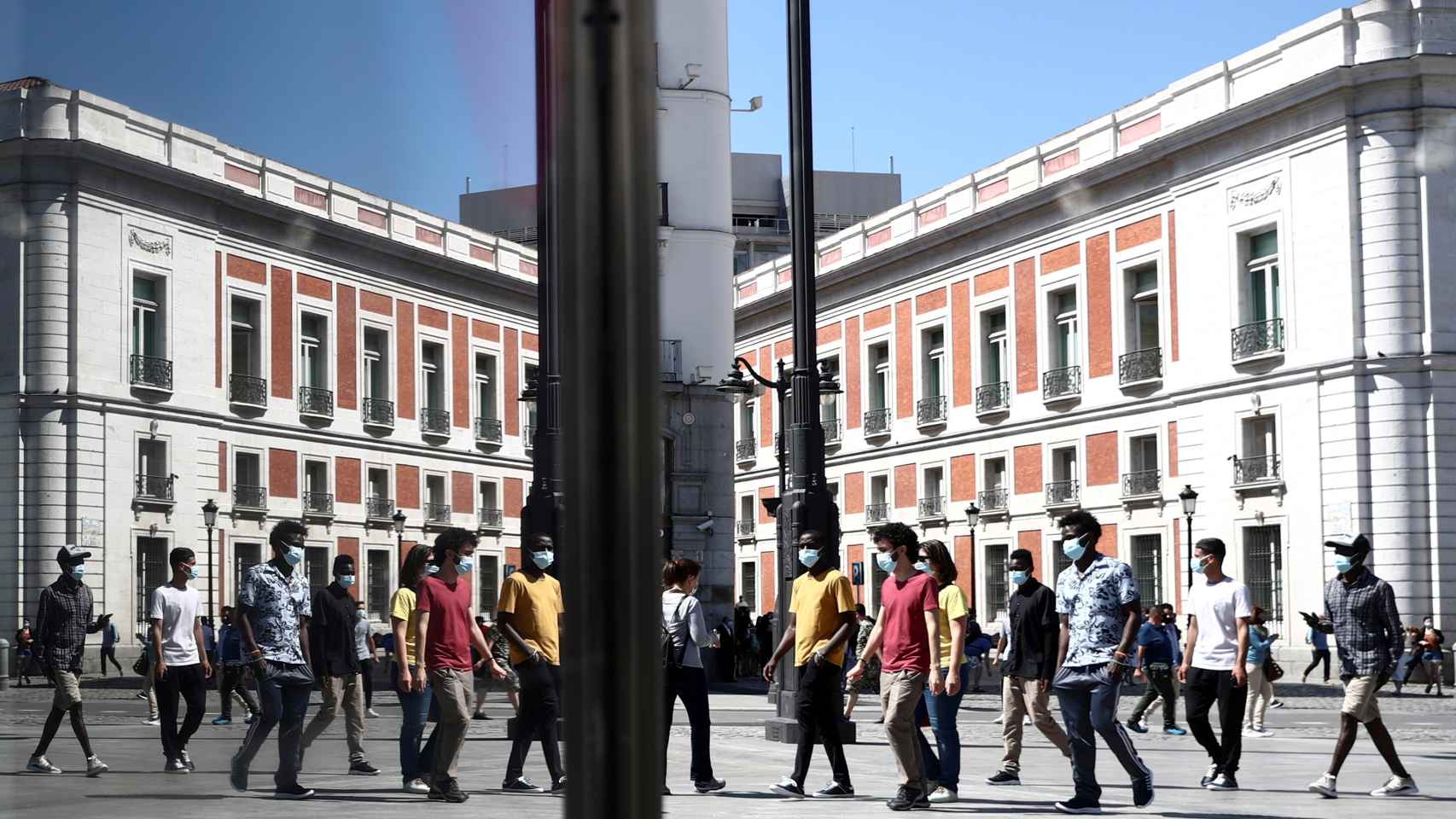 Paseantes con mascarilla reflejados en los escaparates de la Puerta del Sol.