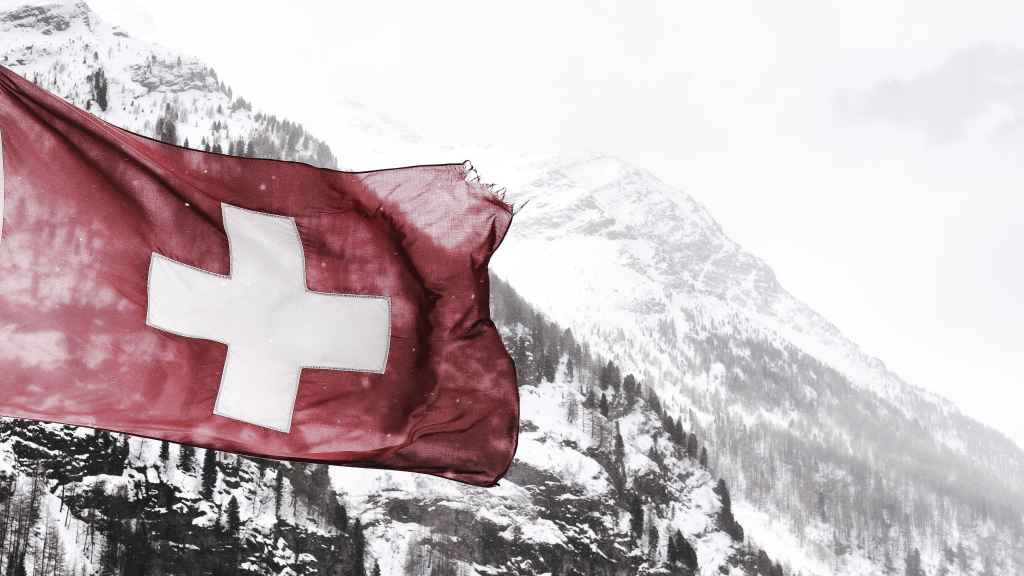 La bandera de Suiza con las montañas nevadas al fondo.