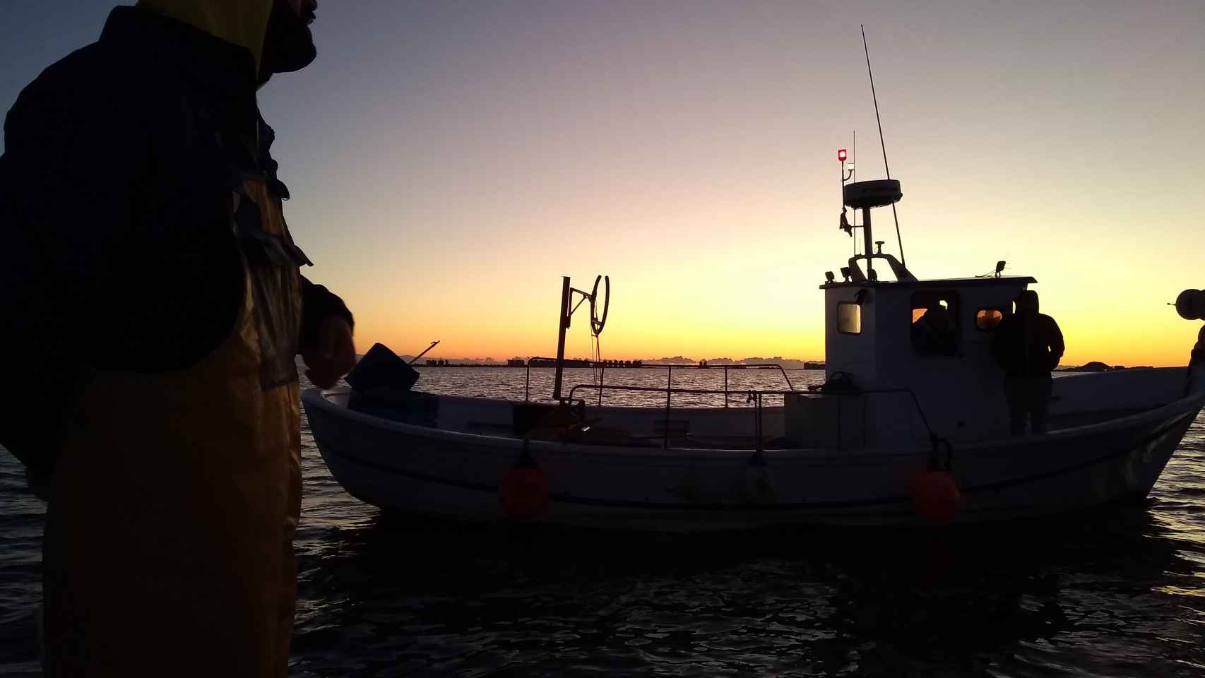 'Al amanecer': Los primeros rayos de sol que bañan el Mar Menor dibujan la silueta de Manolo, patrón de la 'Begoñita', charlando con otros pescadores que han salido a pescar lubina mediante métodos tradicionales.