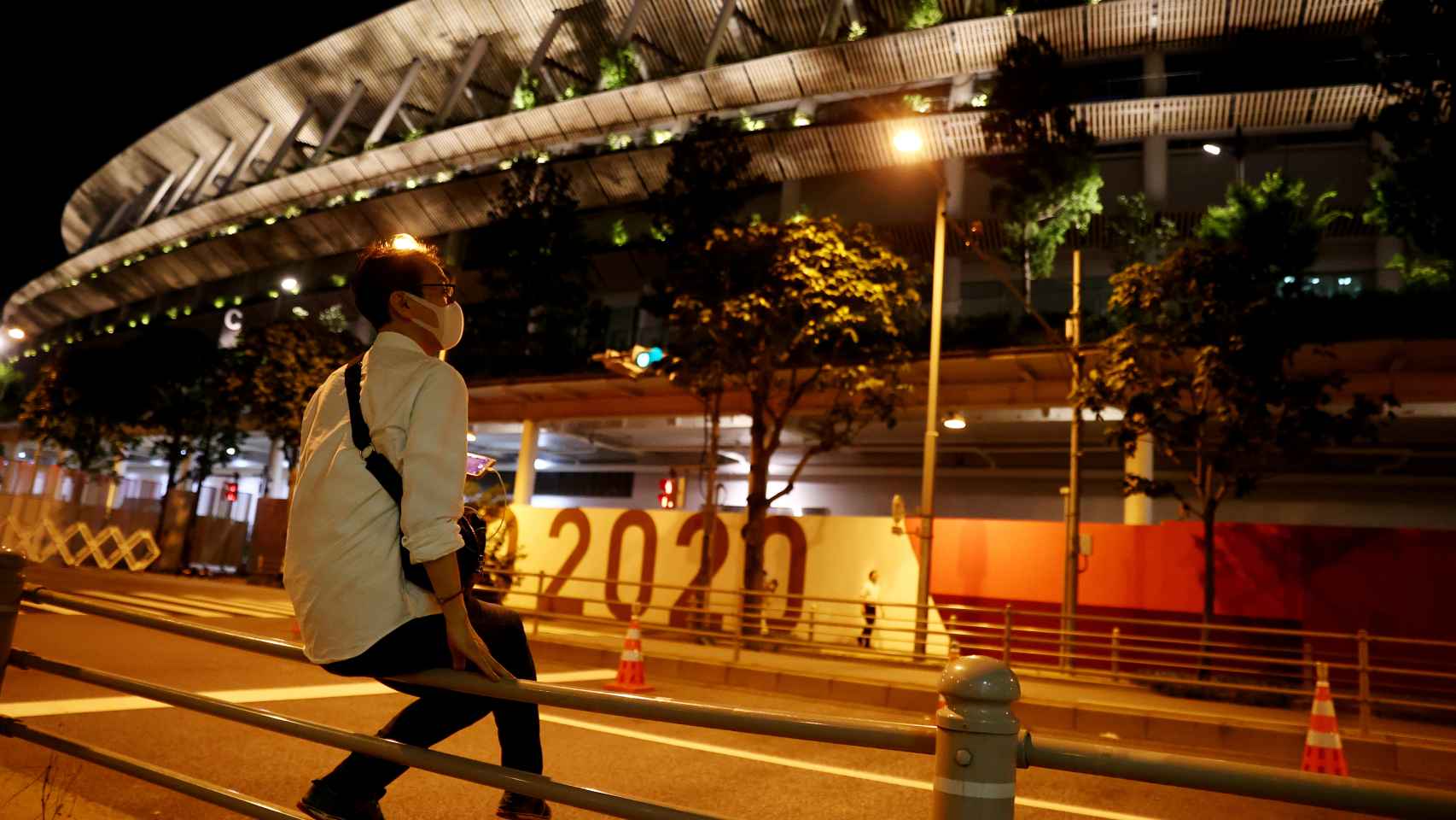 Un hombre llevando una máscara apoyado en frente del Estadio Nacional de Tokio