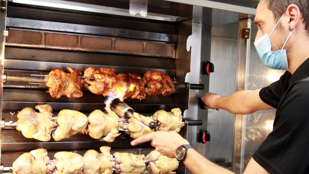 Un trabajador de Casa Galván vigila que los pollos asados queden bien hechos.