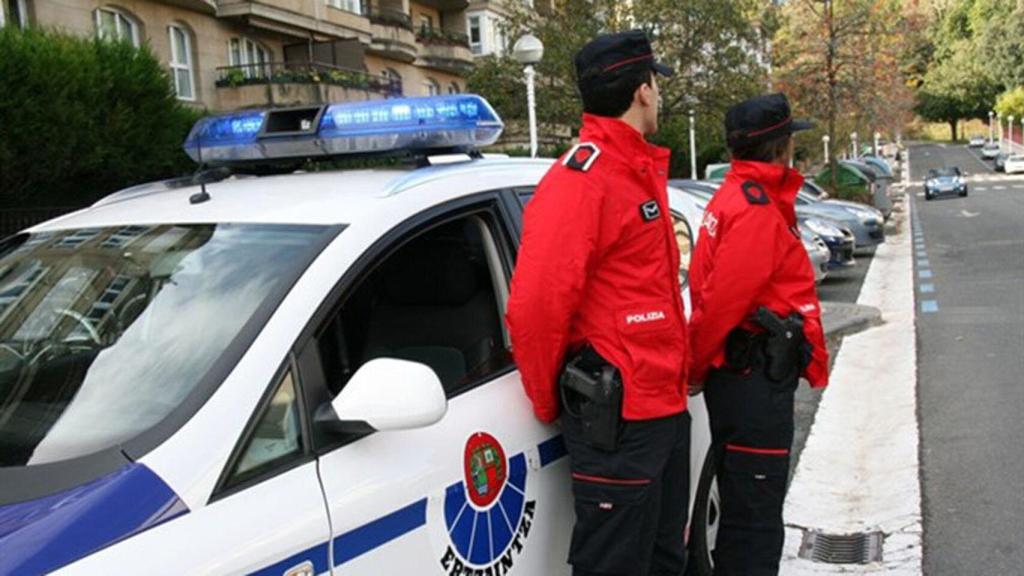 Dos agentes de la Ertzainza, junto a su vehículo.