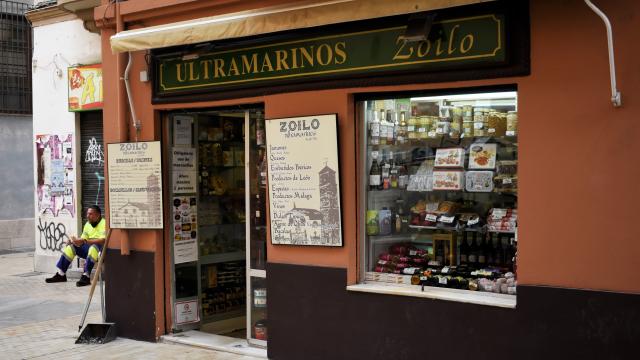 Uan foto de la fachada de Ultramarinos Zoilo. Detrás un trabajador come un bocadillo de la tienda.