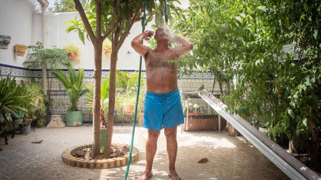 El hombre cuelga la manguera de un níspero, en el centro del patio.