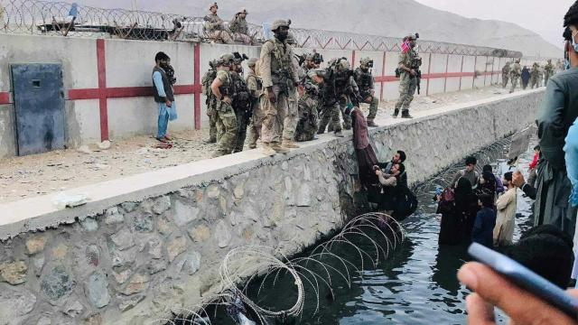 Varios afganos sortean el foto de agua que rodea un lateral del aeropuerto de Kabul, para huir del país.