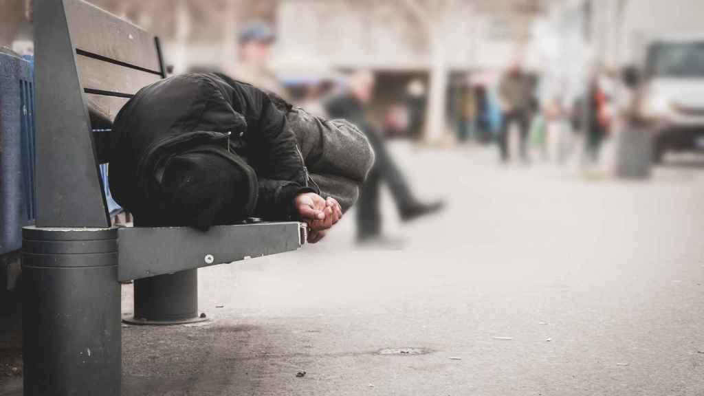 Una persona durmiendo en un banco en la calle, en una foto de archivo