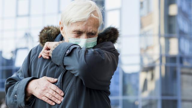 Un hombre tose sobre su codo con la mascarilla puesta.