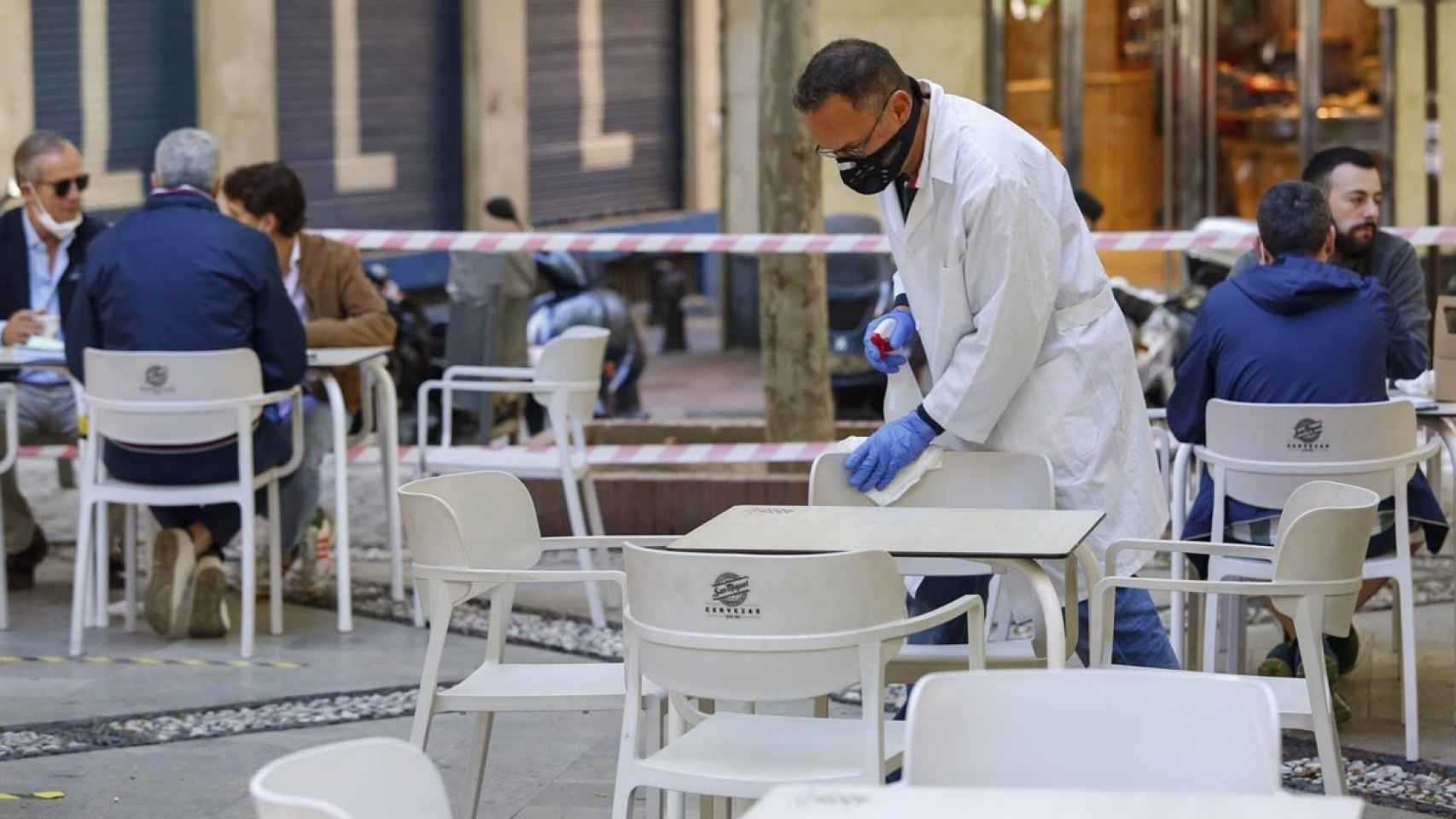 El trabajador de un bar limpia las sillas de una terraza en Málaga.