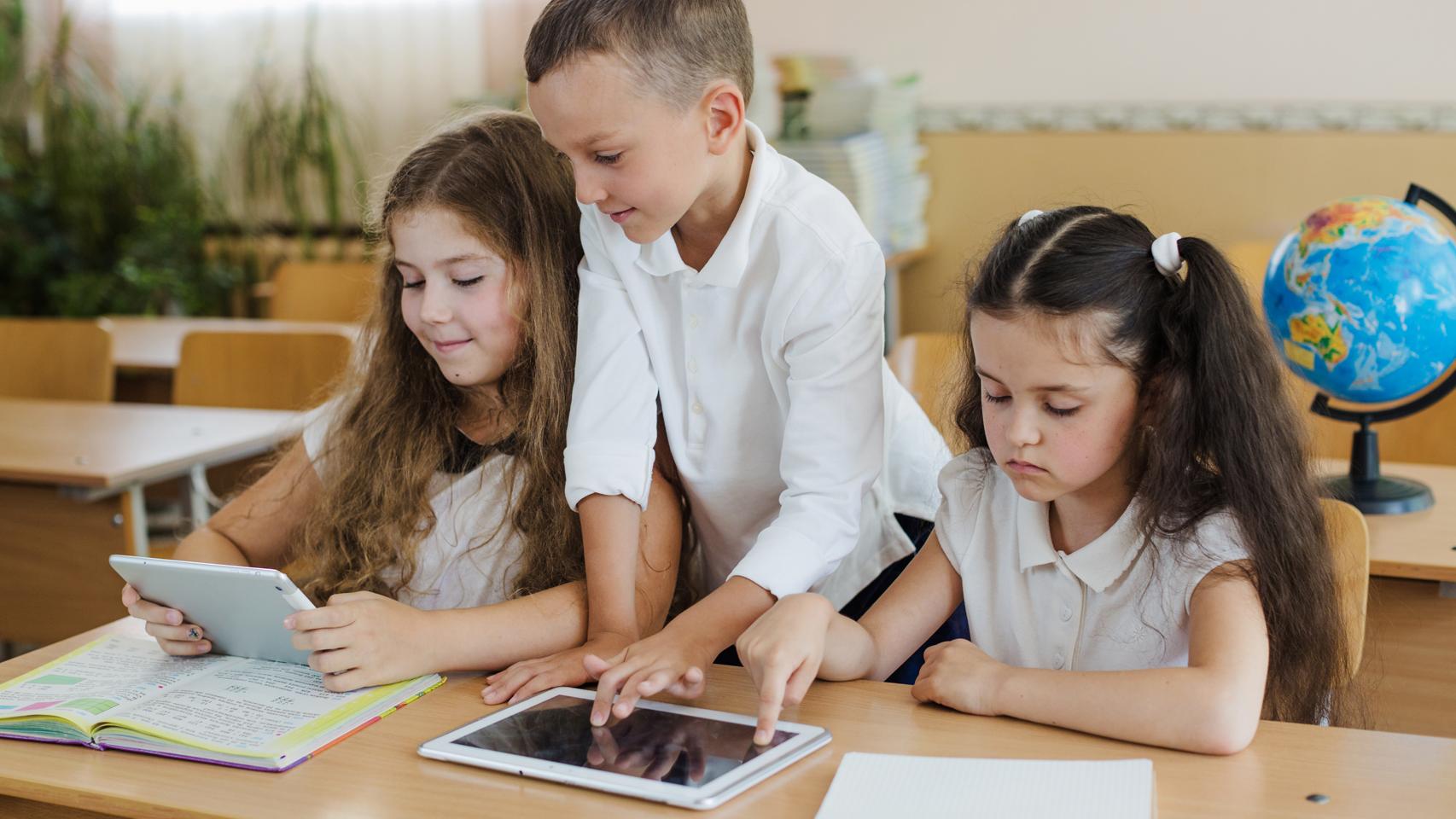 Estudiantes en clase usando libros y tabletas.