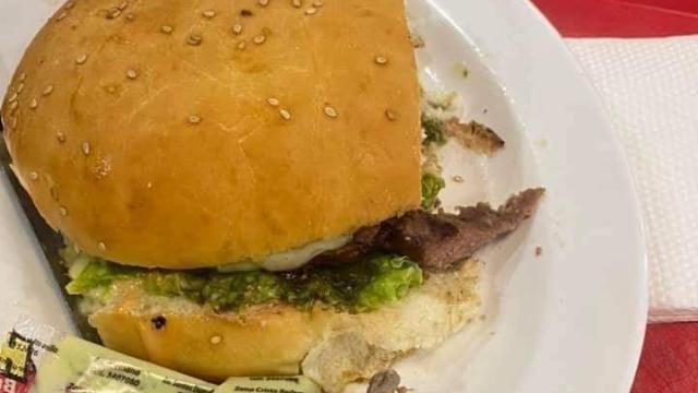 La hamburguesa en cuestión con el dedo en el plato.