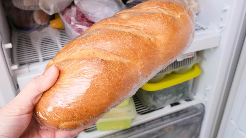 Una persona coloca una barra de pan en el interior del congelador.