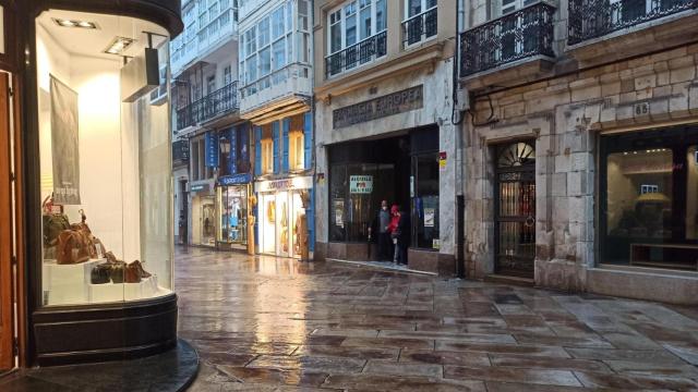 Dos personas se resguardande la lluvia en un local de la calle Real.