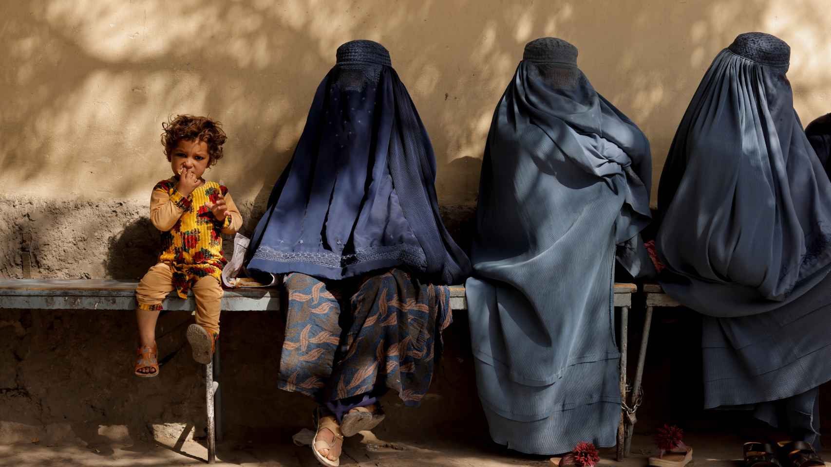 Una niña junto a tres mujeres cubiertas por burkas sentadas afuera de un hospital de Kabul, Afganistán.