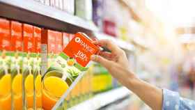 Una mujer compra un brick de zumo de naranja en el supermercado.