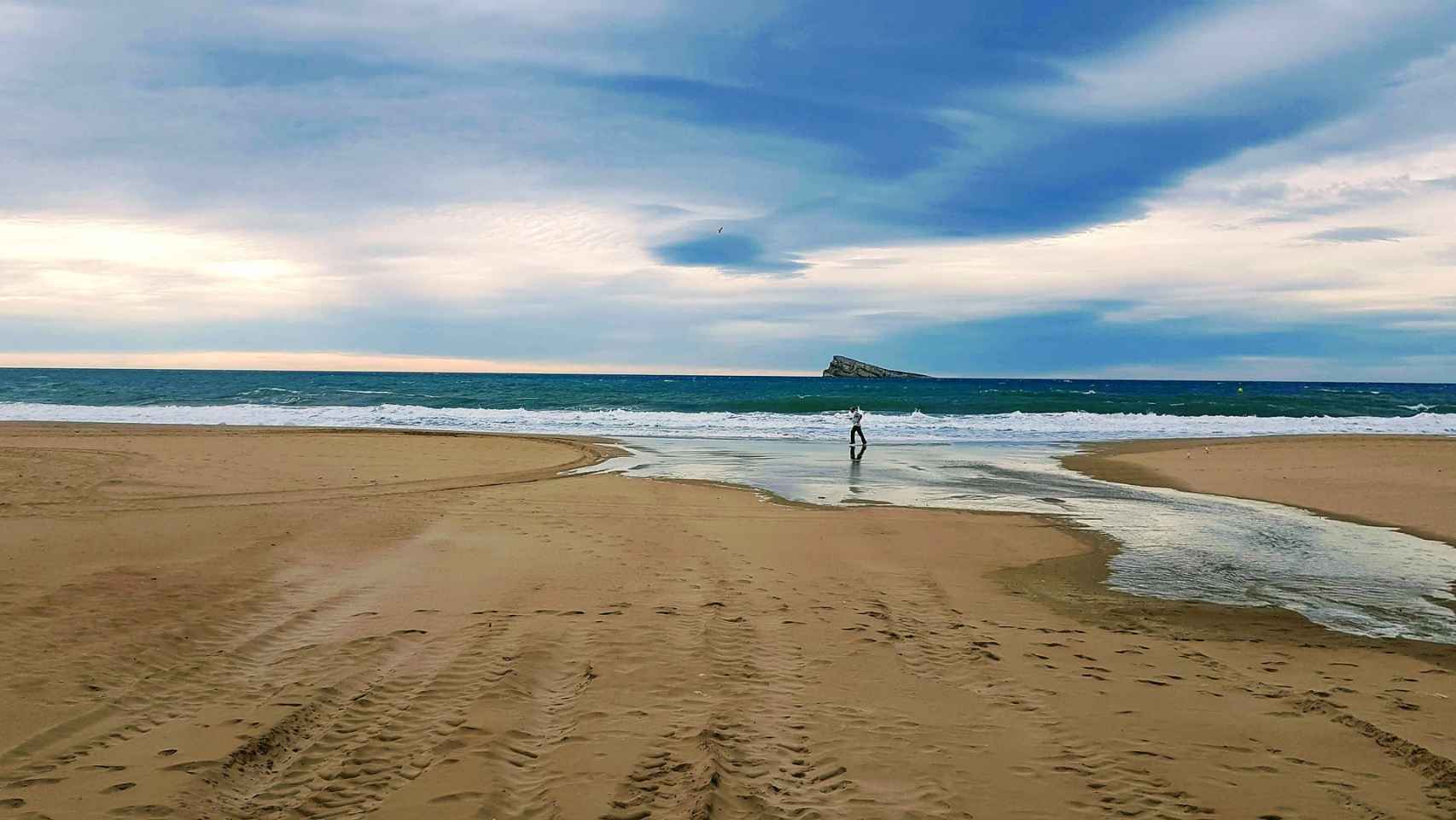 Una persona hace deporte por la playa frente a la Illa de Benidorm.