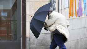 Un viandante sujeta con fuerza su paraguas ante el viento.