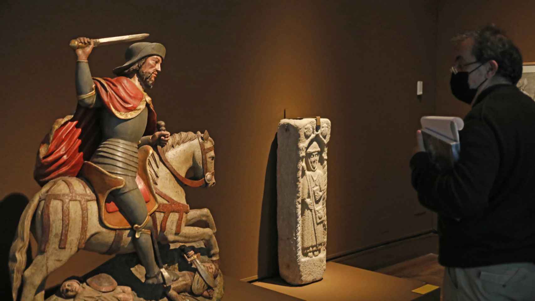 Un visitante junto a una estatua del apóstol y un bajorrelieve de un peregrino.