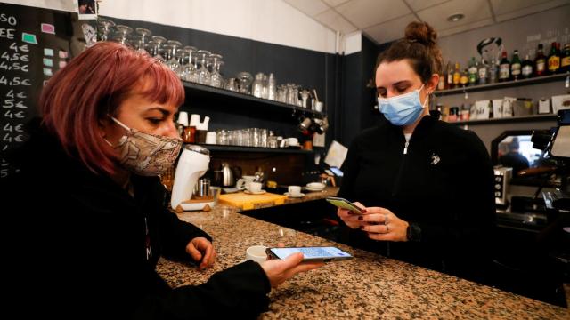 Una mujer enseña el certificado de vacunación en una cafeteria.