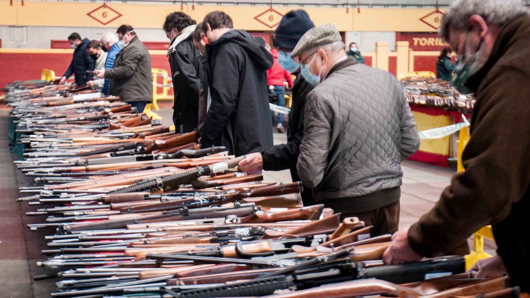 Varias personas ojean las escopetas de caza expuestas en la plaza de toros de Moralzarzal.