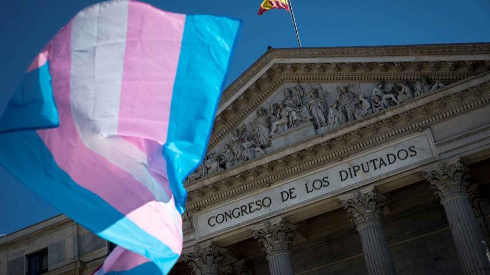 Una bandera trans ondea ante el Congreso de los Diputados.