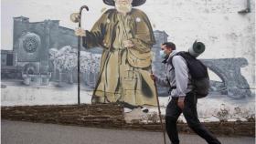 Un peregrino pasa ante un mural de Zapatones en Lugo.