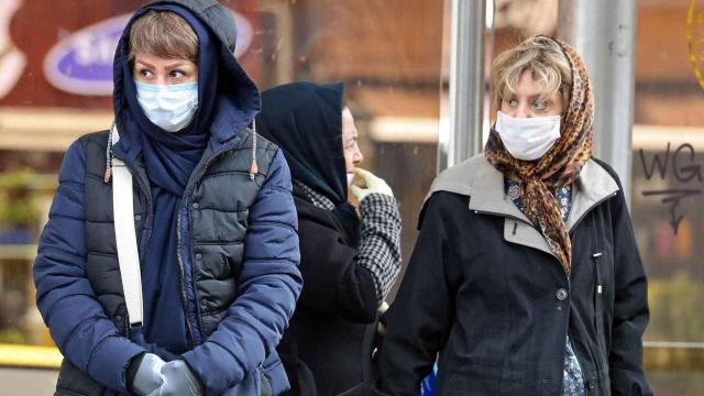 Mujeres con mascarilla esperando en una marquesina.