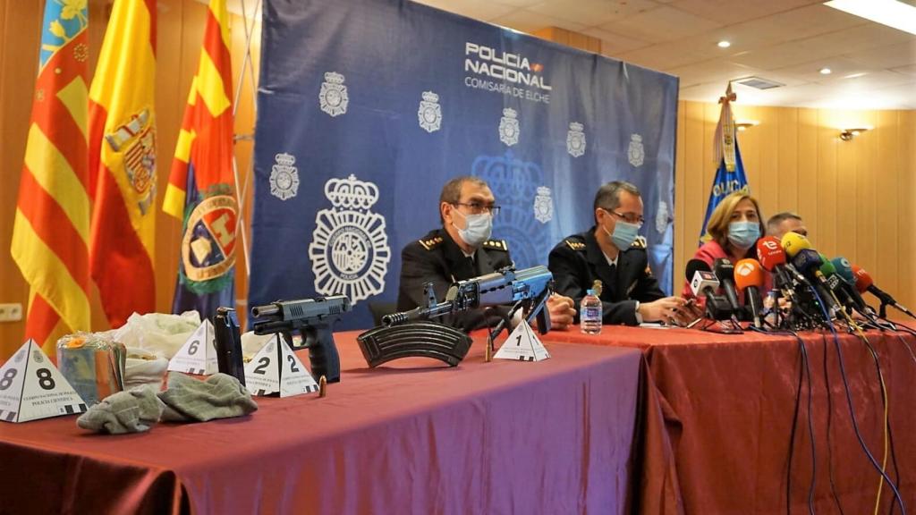 El detenido, a la izquierda, en su llegada a la Comisaría de Elche, donde se han expuesto las armas intervenidas.